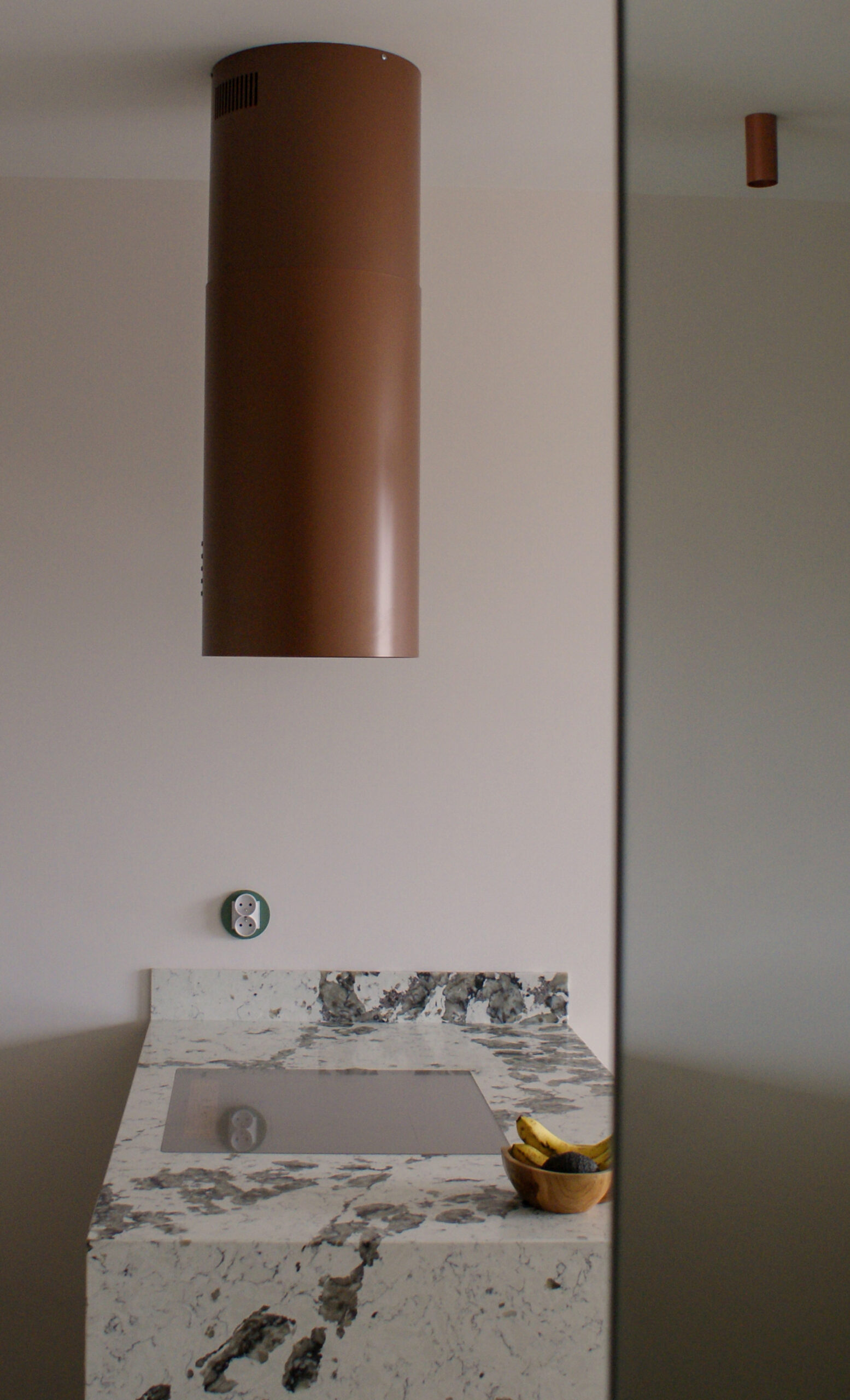 Miedziany okap tuba nad wyspą kuchenną. Widoczny fragment blatu Patagonia i zabudowa kuchenna pod sufit.